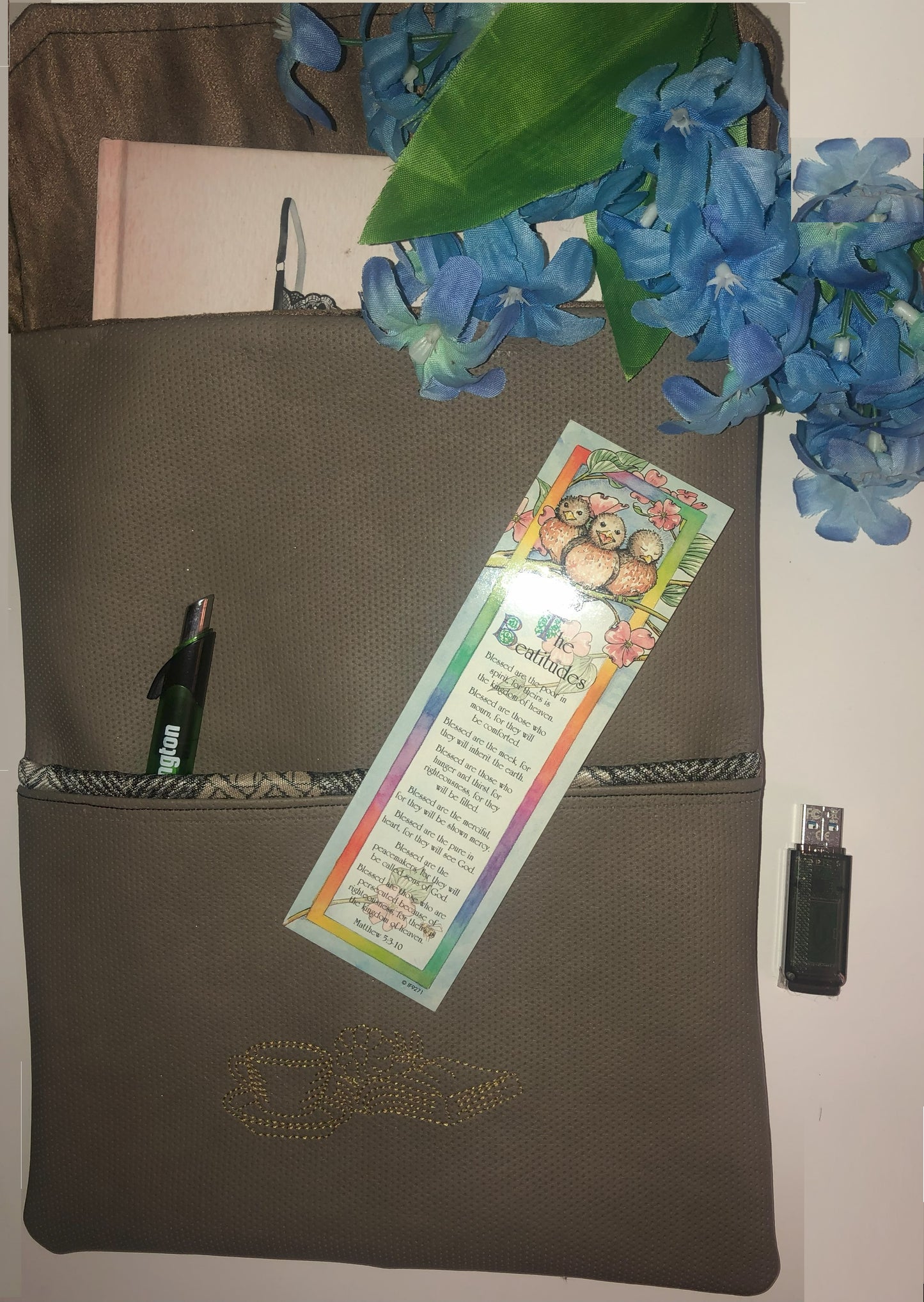 Faux Leather Book Sleeve with Outside Pocket. Embroidery Design - Coffee Cup and Book with Flower. With arched wording - "Read More Books" Color Taupe with beigh and cream jacquard loom print fabric closure and pocket trim.